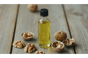 Cold pressed walnut oil in a glass bottle with whole walnuts and cracked walnut shells on a wooden surface