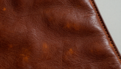 A close-up of full-grain aged leather showing rich natural patina, unique texture, warm tones, and natural creases formed through years of use and craftsmanship