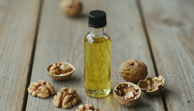 Cold pressed walnut oil in a glass bottle with whole walnuts and cracked walnut shells on a wooden surface